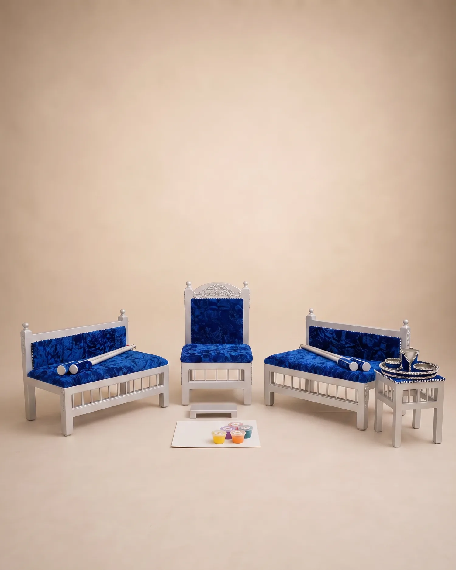 The Blue Prince Maiyan suite on a warm ivory studio backdrop: silver-grey slatted frames with royal blue crushed velvet seats, the carved head chair between two benches, with the tray table and beaded Sagan tray alongside.