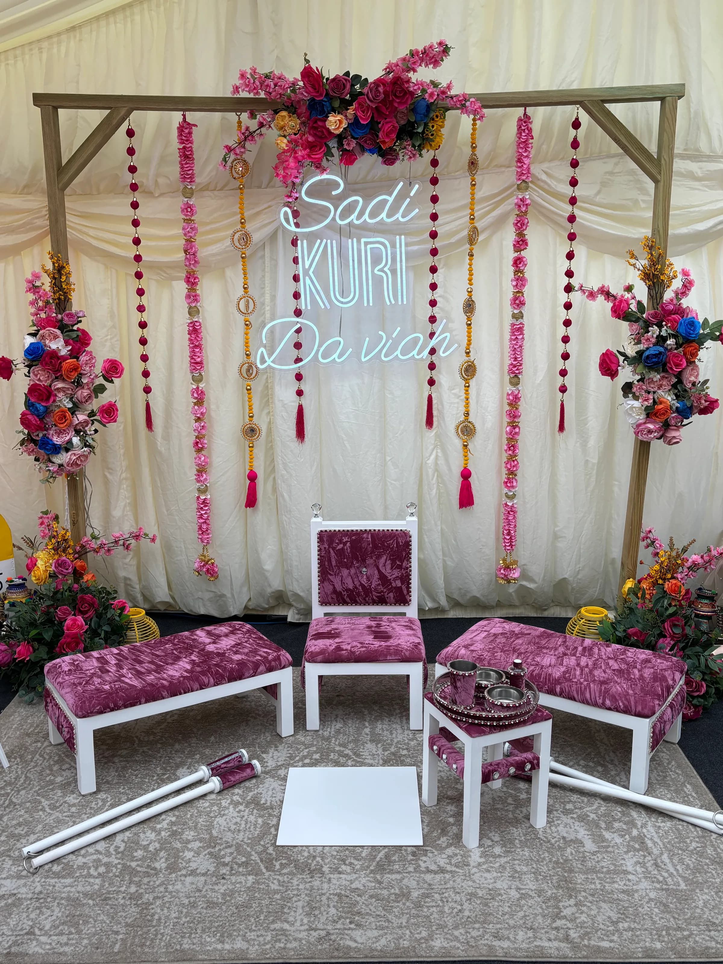A Rose Quartz style suite in white and plum velvet set up in a marquee beneath an illuminated “Sadi Kuri Da Viah” sign.
