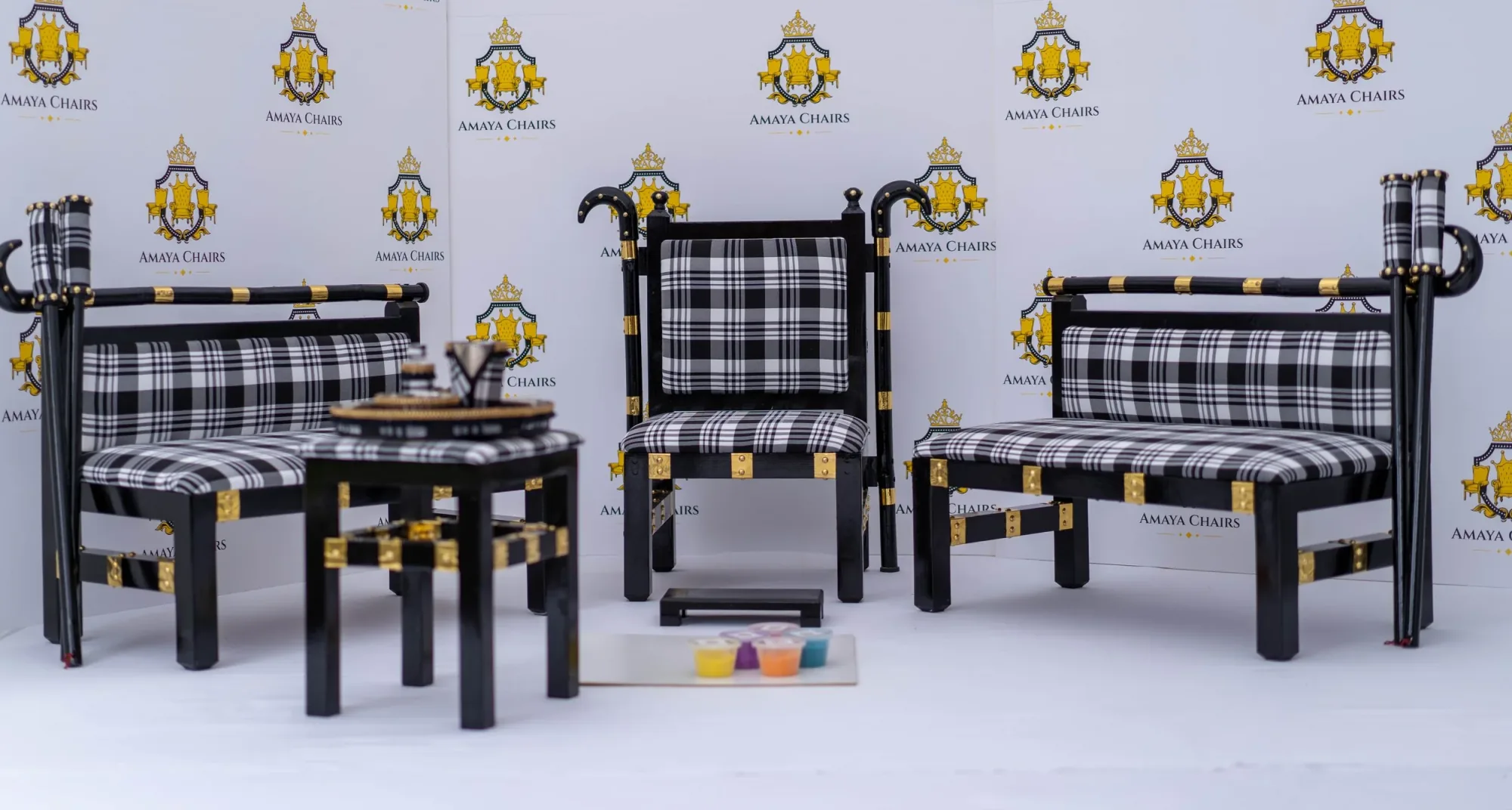The Gabru suite photographed in full against the Amaya Chairs backdrop: black lacquered head chair between two check-upholstered benches, with the tray table alongside.