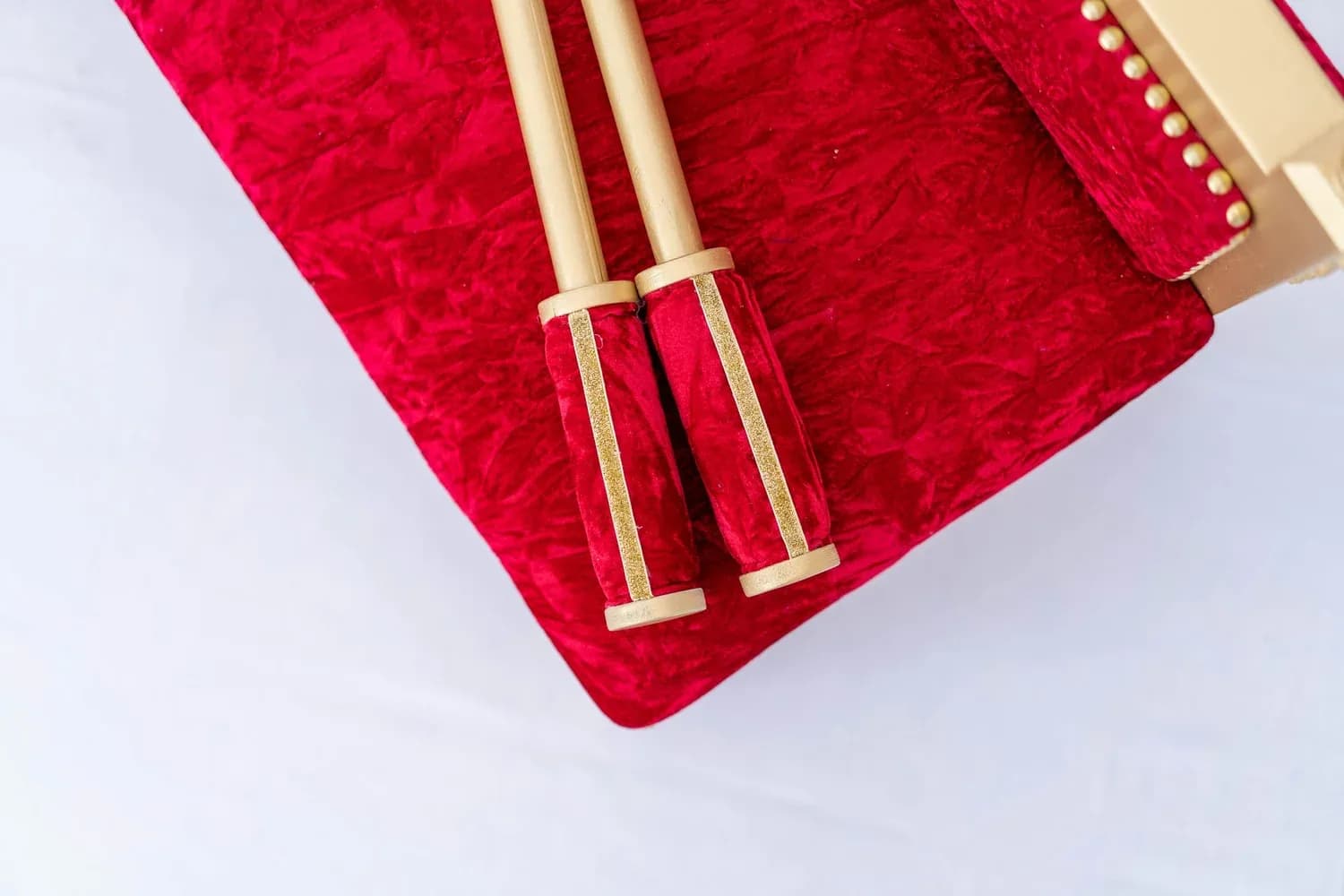 A close view of the Royal Crimson chunni sticks — gold-bound and wrapped in crimson velvet — laid across the matching Phatti.